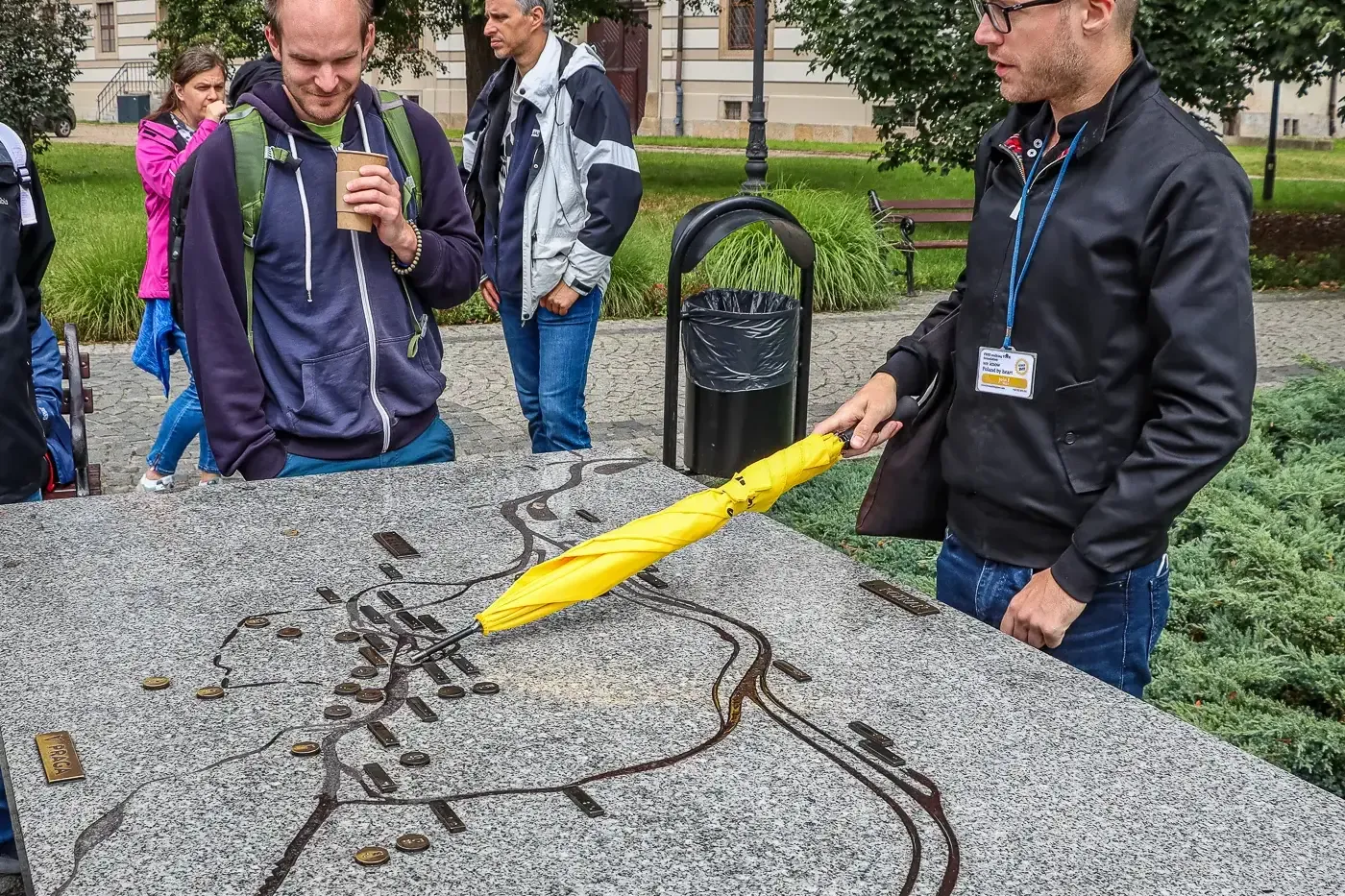 Tour guide with a yellow umbrella pointing at a tactile map of Wrocław while a small group of tourists listens.