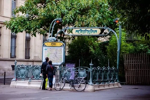 Art Nouveau Paris Métro entrance for Cité station with two people looking at a map and a bicycle parked nearby.