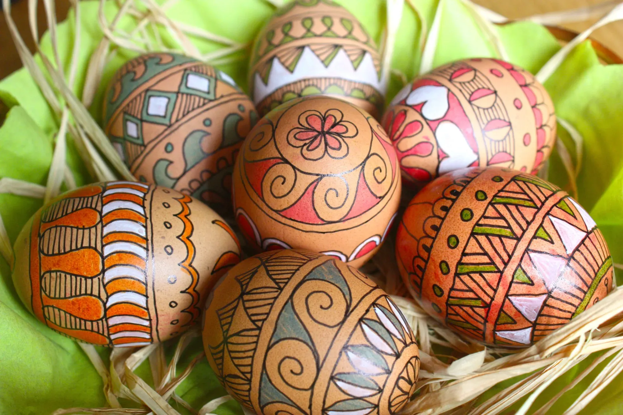 Close-up of traditional hand-painted Easter eggs resting on light green fabric and dry straw.