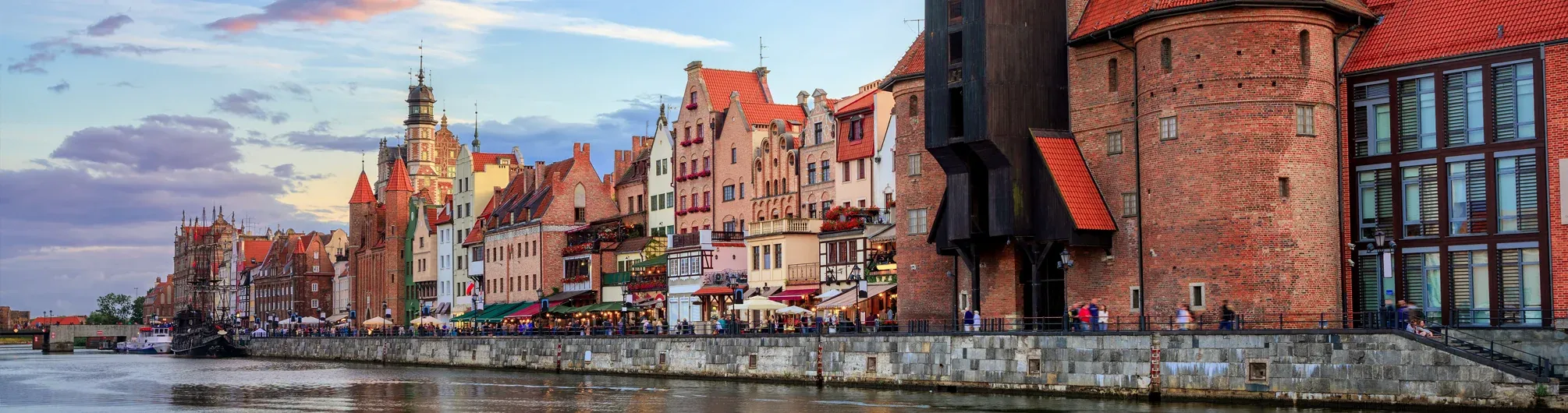 Historic waterfront of Gdansk on the Motława River with the iconic Żuraw crane, colorful merchant houses, and people walking.