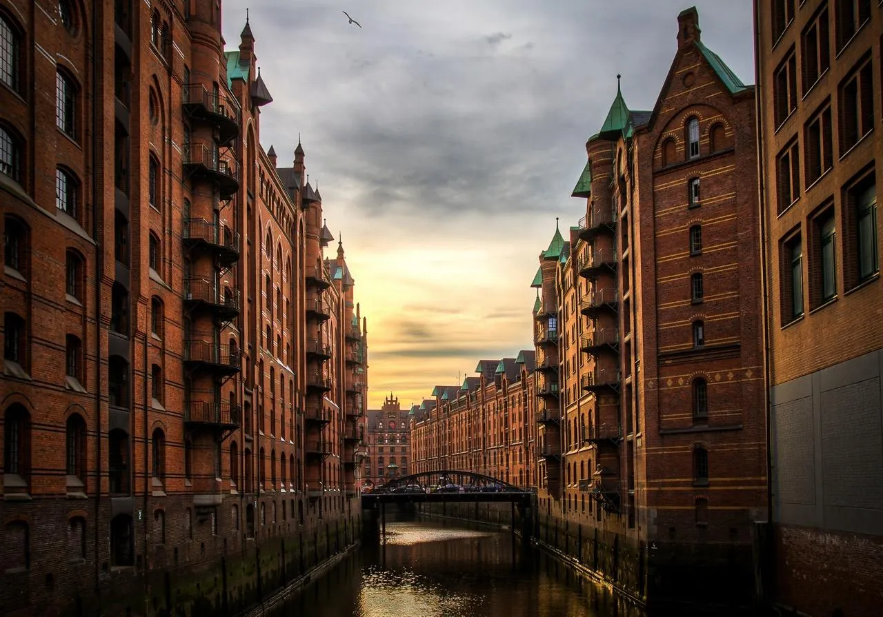 Historic brick warehouses with green roofs line a canal at sunset in Hamburg's Speicherstadt district.