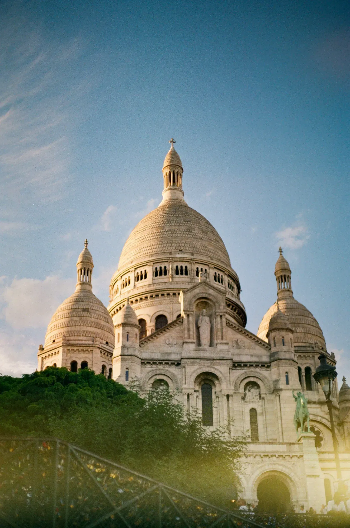 The Sacré-Cœur Basilica with its white domes and facade, seen from below at sunset.
