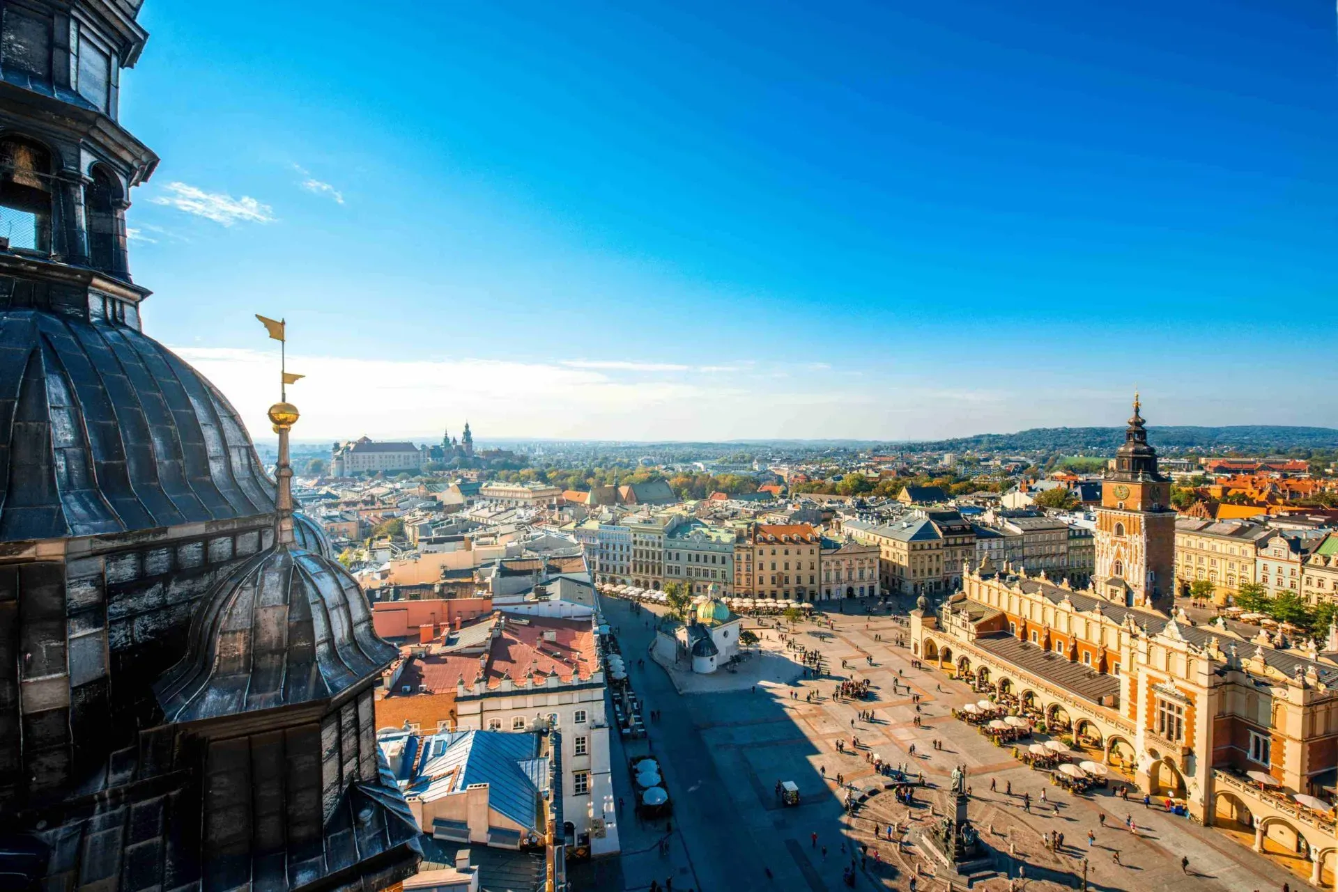Aerial view of Krakow's Main Market Square with Cloth Hall, St. Mary's Basilica tower, and Wawel Castle in the distance.