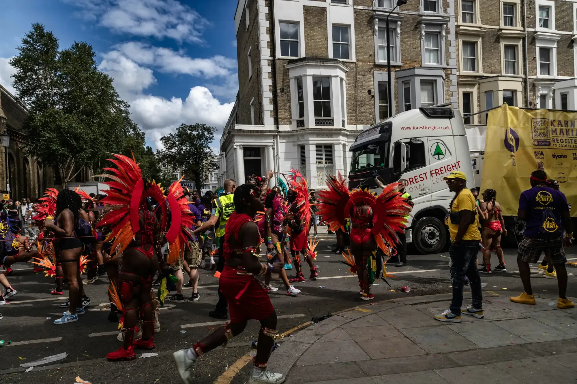 Dancers in vibrant red feathered costumes parade down a London street during the Notting Hill Carnival.