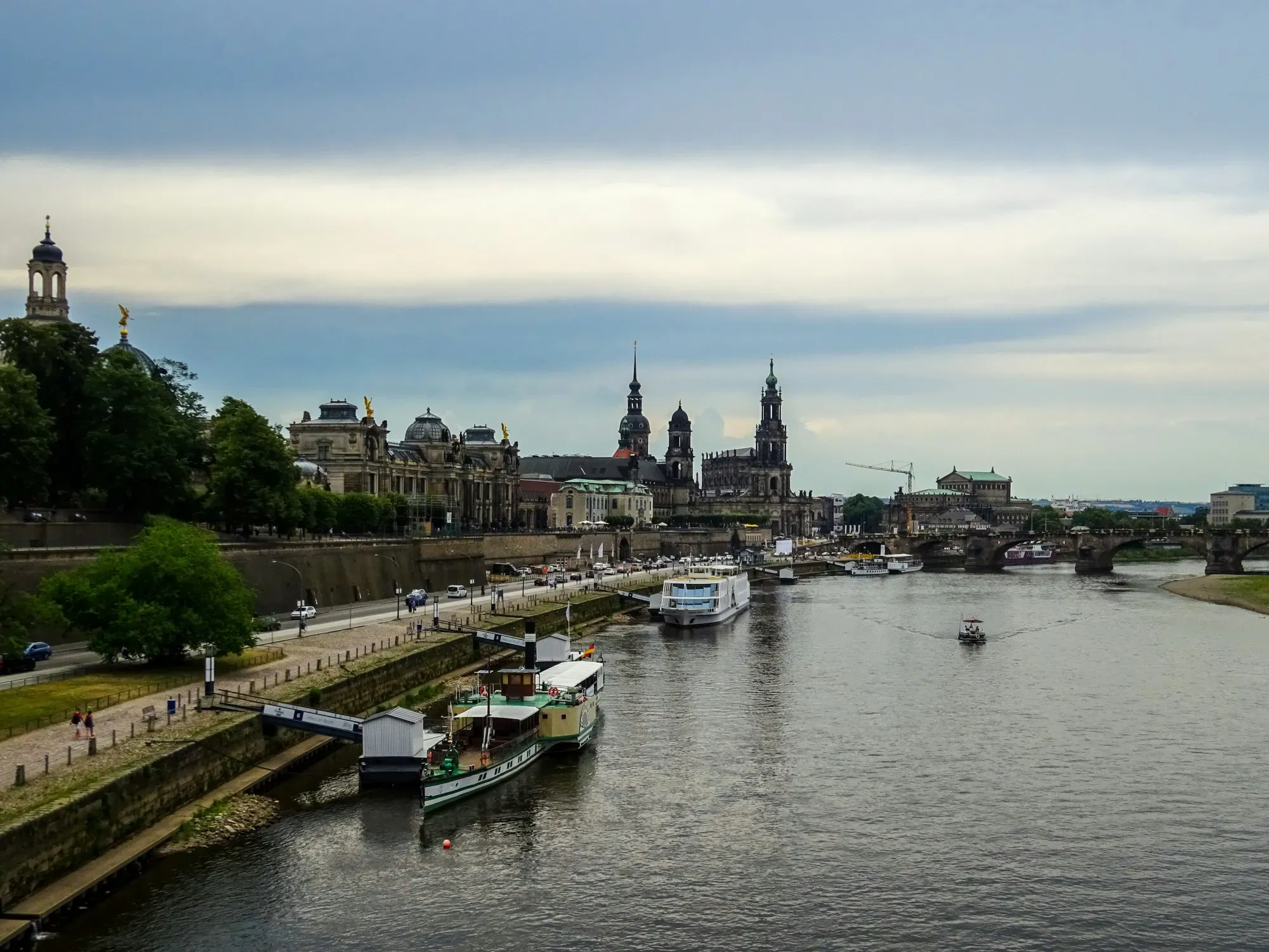 Dresden's historic skyline with the Elbe River in the foreground, under a cloudy sky.