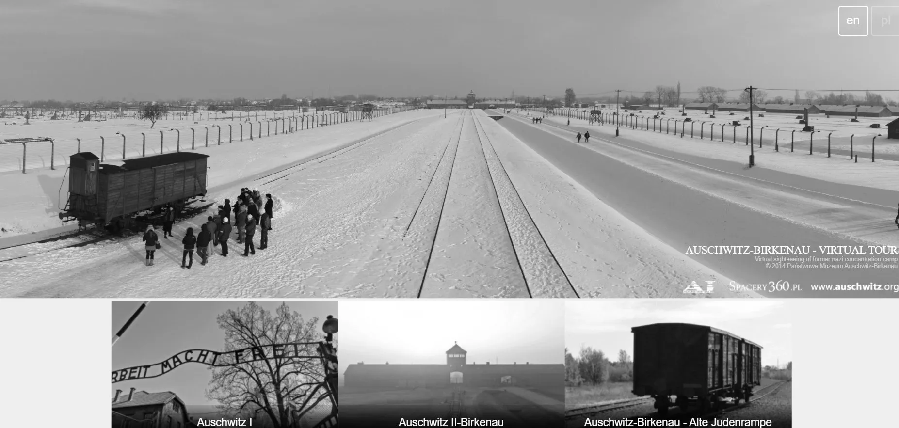 Snow-covered railway tracks at Auschwitz-Birkenau concentration camp with a wooden freight car, people, fences, and distant g