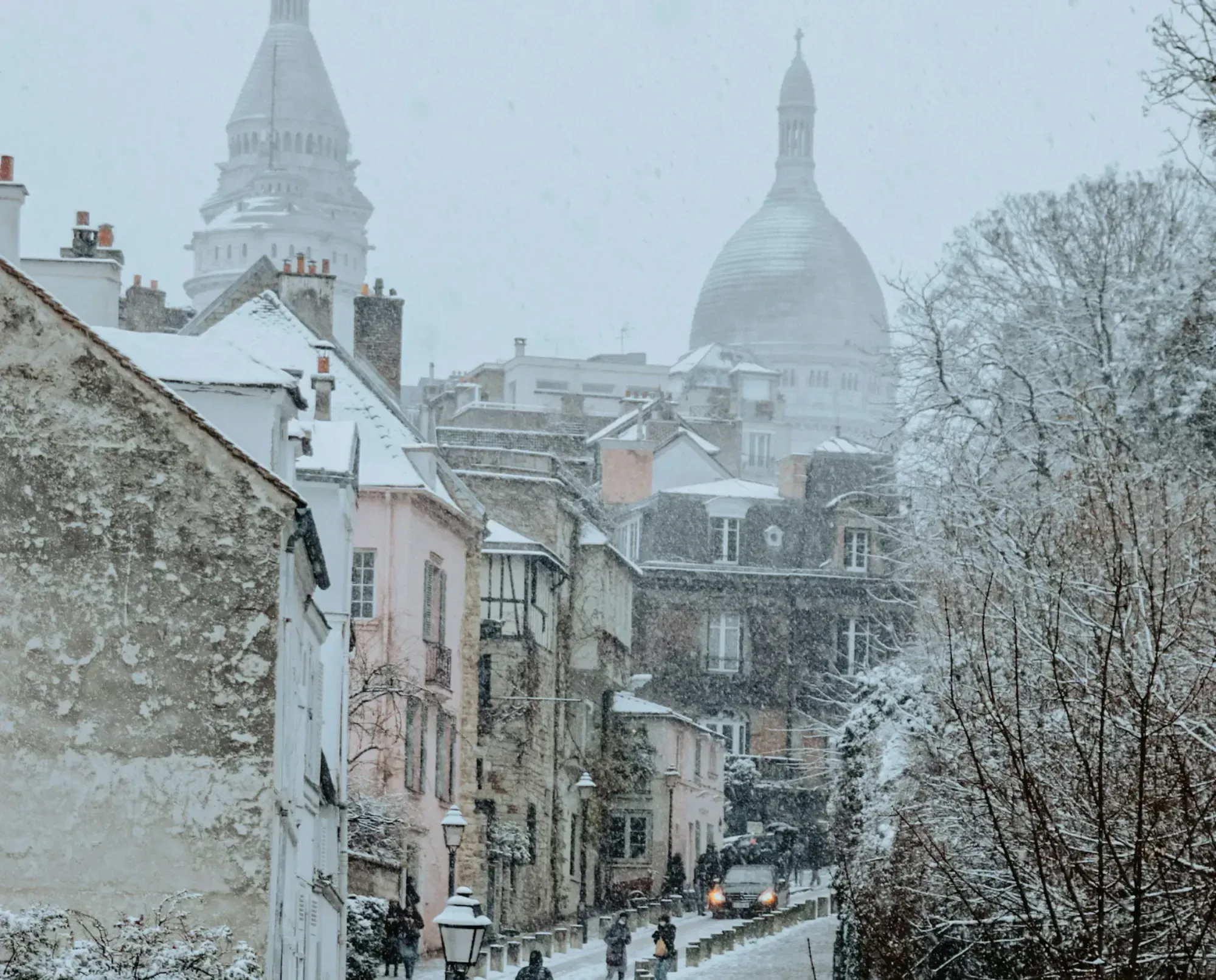 Snow-covered Montmartre street with Sacré-Cœur Basilica domes visible through the snowfall.