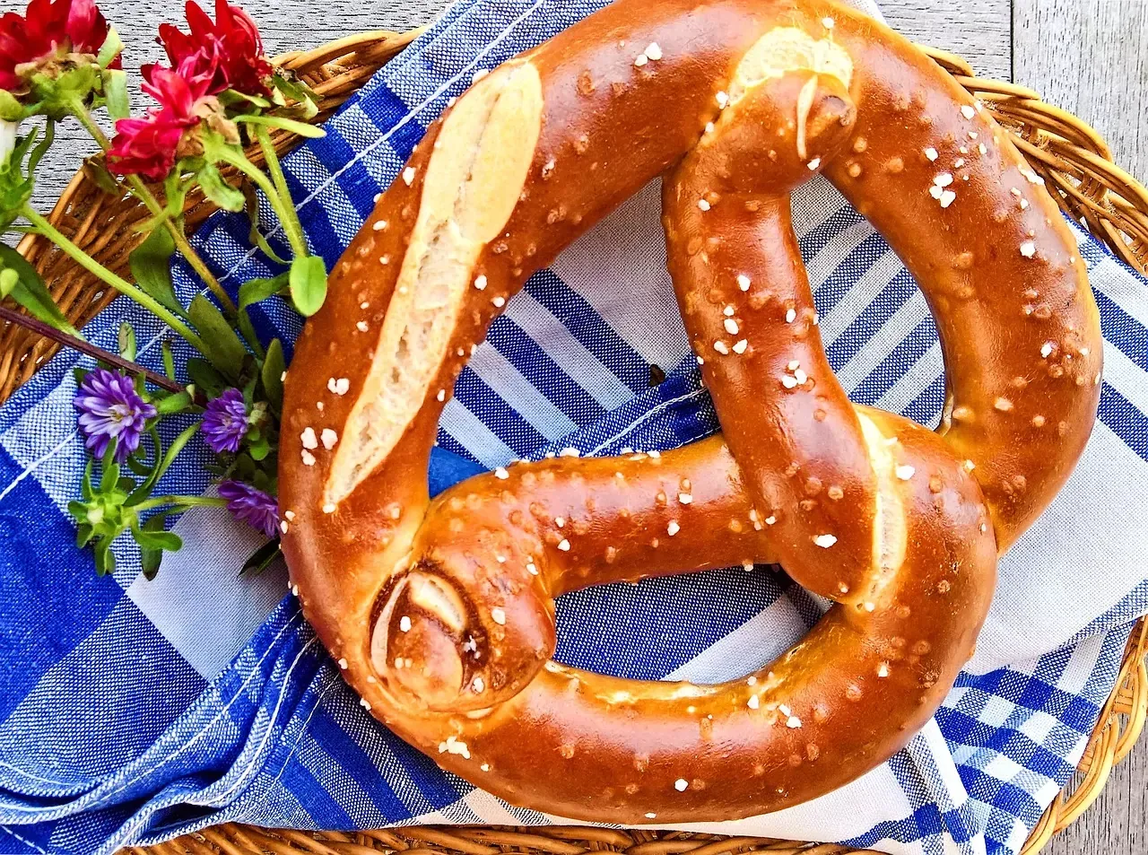 Large, golden-brown Bavarian pretzel with coarse salt crystals, on a blue and white checkered napkin in a wicker basket with