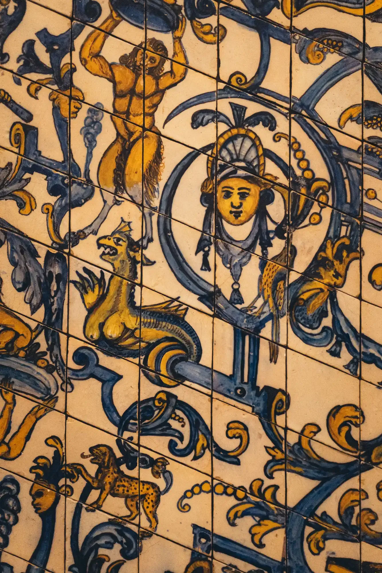 Close-up of yellow and blue decorative ceramic tiles with mythological figures including a satyr, a dragon, and a leopard.