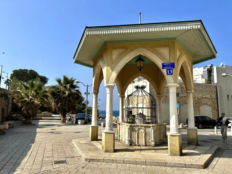 A historical water fountain in a sunlit square in Acre, Israel.