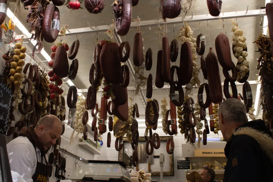 A vibrant Greek market stall overflowing with hanging cured meats and sausages.
