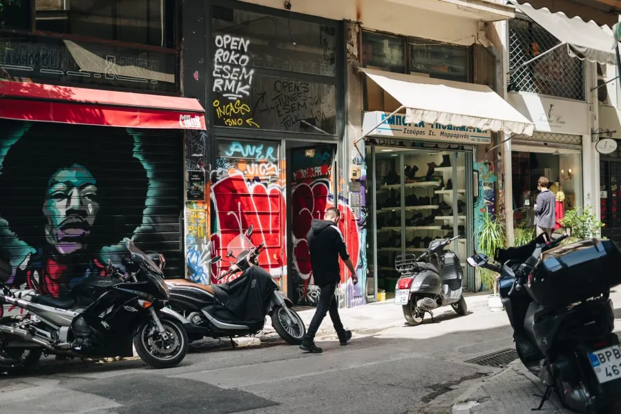 A vibrant street scene in Athens, Greece, featuring colorful graffiti and parked scooters.