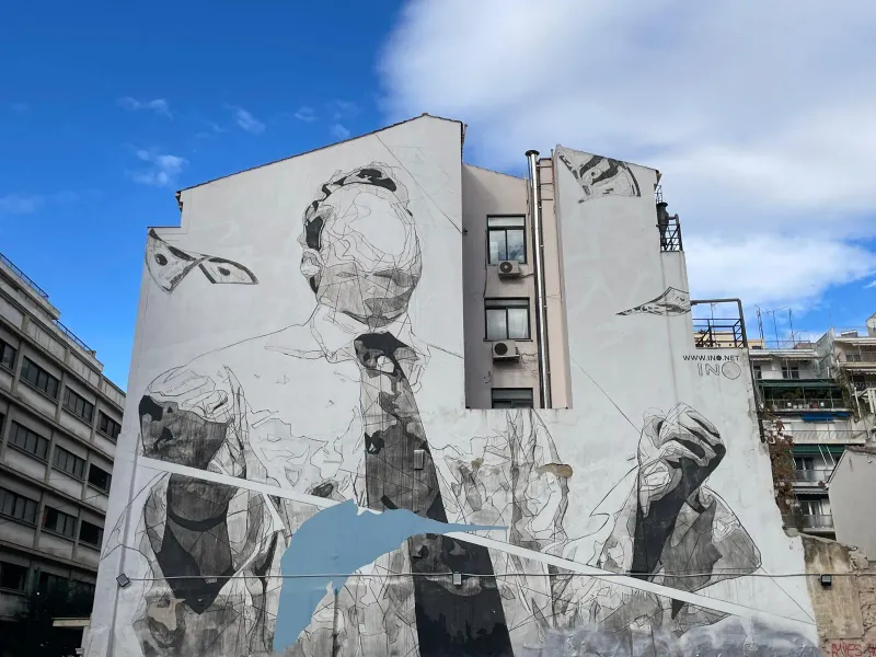 A large grayscale mural of an abstract figure adorns a building in Athens, Greece.
