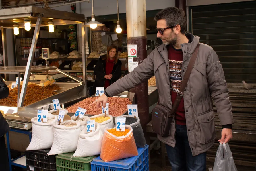 A tour guide shows tourists various legumes and nuts at a vibrant market in Athens, Greece.