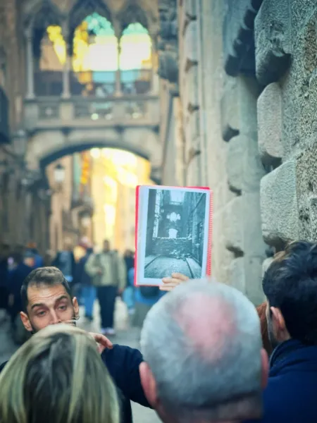 A tour guide in Barcelona's Gothic Quarter shows a historical photo to a group.