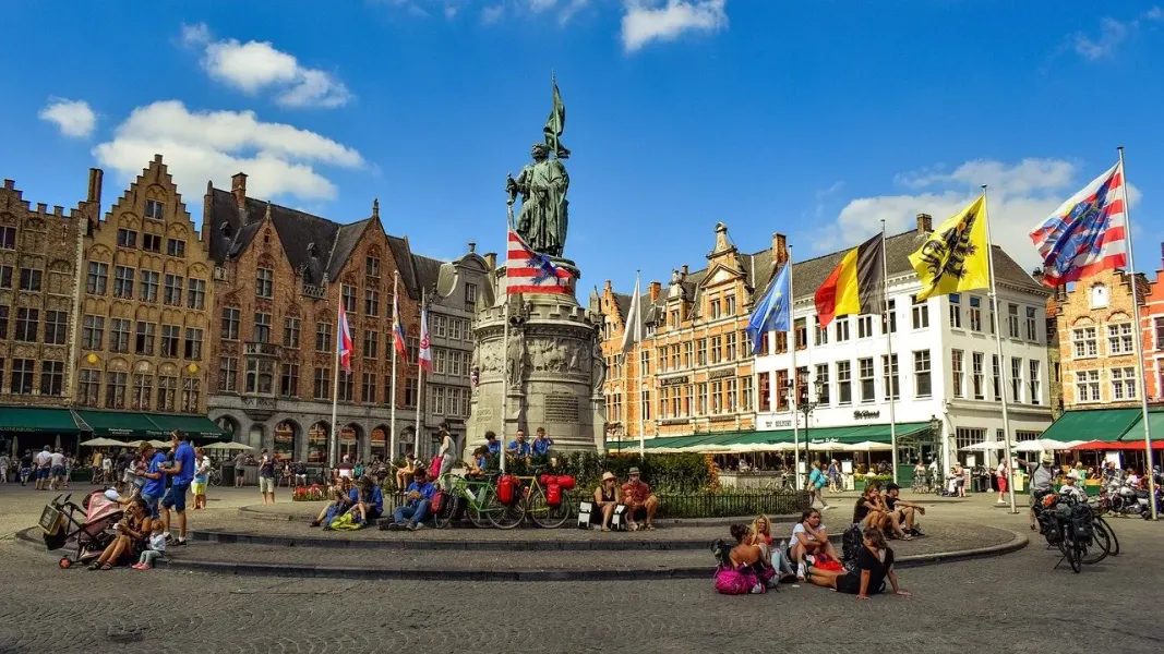 Tourists enjoying the Market Square in Bruges, Belgium, with the Jan van Eyck statue in the background.