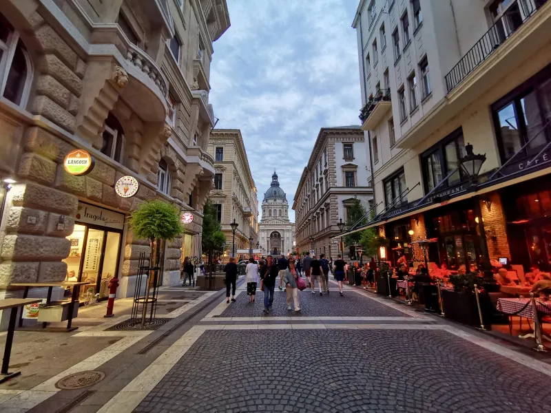 Tourists walking down a charming cobblestone street in Budapest, Hungary, with St. Stephen's Basilica in the background.