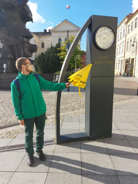 Tourist exploring a unique clock installation in Bydgoszcz, Poland.