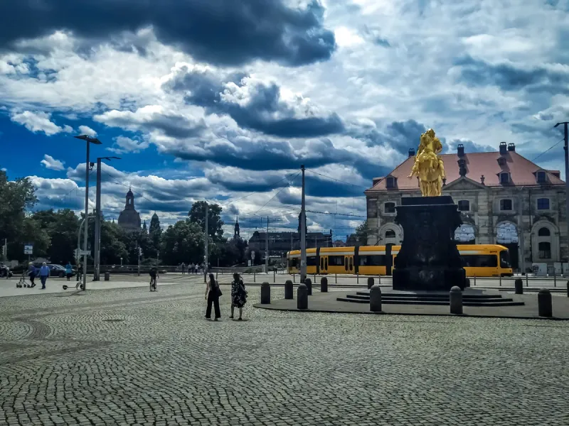 The Golden Horseman statue in Dresden's cobblestone square, with a tram and city skyline in the background.