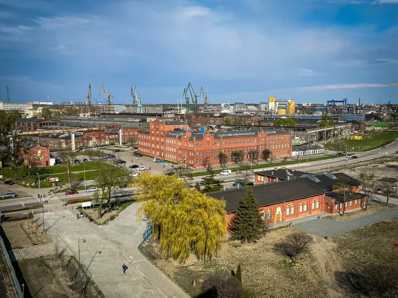 Aerial view of Gdansk's industrial port area, showing red brick buildings and a park.