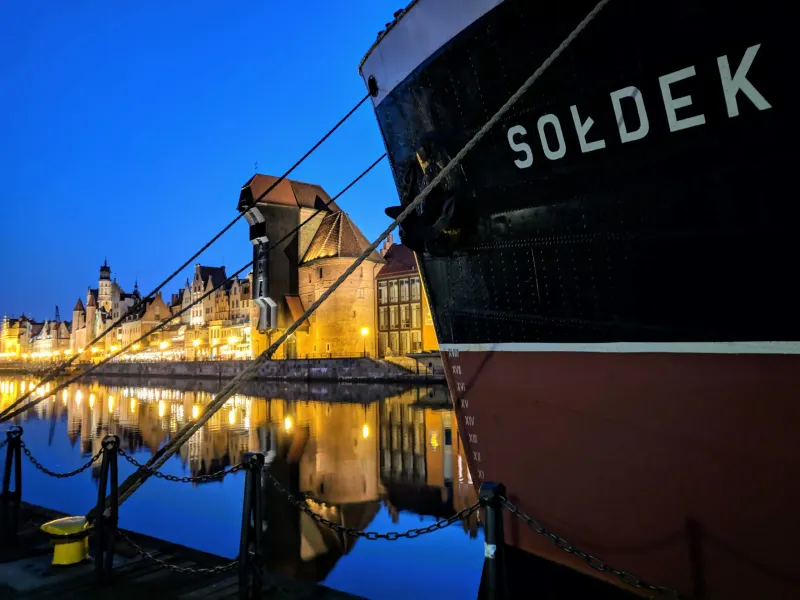 Evening view of Gdansk's Old Town reflected in the Motława River, with the historic ship Soldek in the foreground.