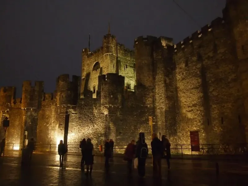 Tourists admiring Gravensteen Castle in Ghent at night.