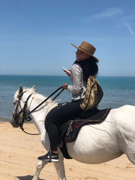 Woman enjoying a horseback riding tour on a beautiful beach.