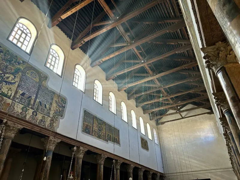 Sunbeams illuminate the majestic interior of a Jerusalem church, showcasing stunning mosaics and wooden beams.