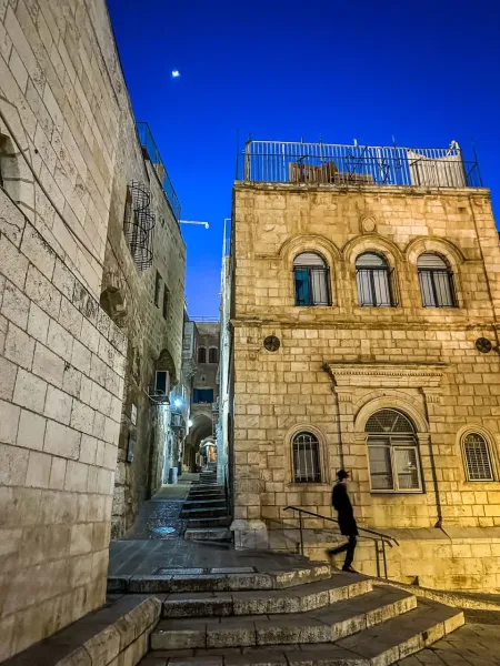 A person walks down a stone staircase in the illuminated Old City of Jerusalem at night.