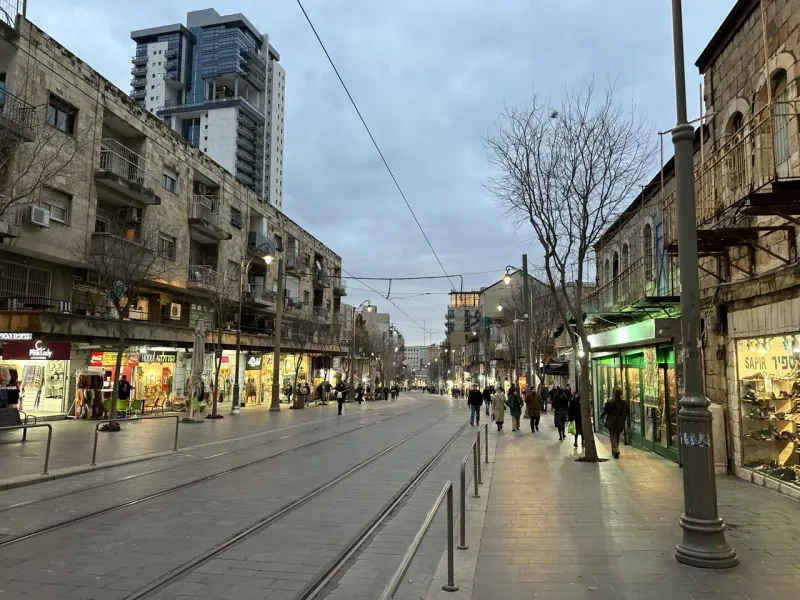 Evening view of a pedestrian street in Jerusalem, with shops and people walking.