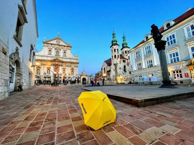 A yellow umbrella with 'Walkative!' in Krakow's Old Town square at dusk.
