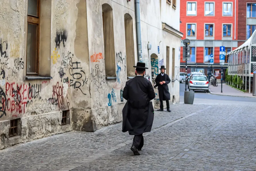 Two men in traditional clothing walk down a cobblestone street in Krakow's Kazimierz district.