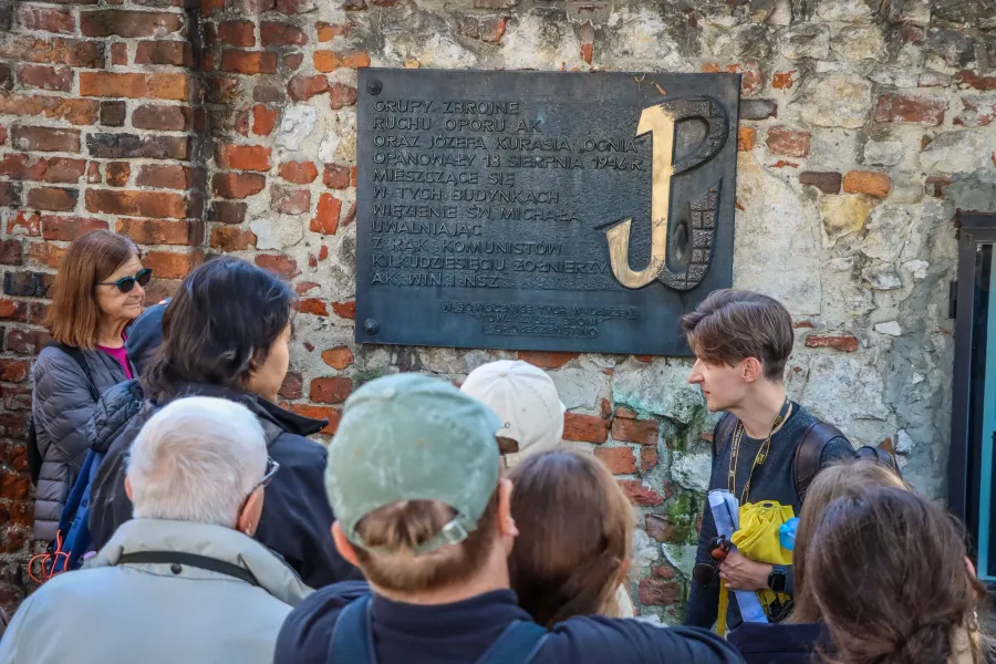 A tour guide leads a group of tourists in Krakow, Poland, in front of a historical plaque.
