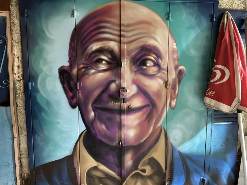 Vibrant street art mural of a smiling elderly man in Lisbon, Portugal.