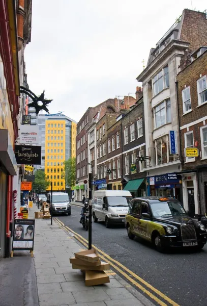 A bustling London street scene with shops and a black cab.