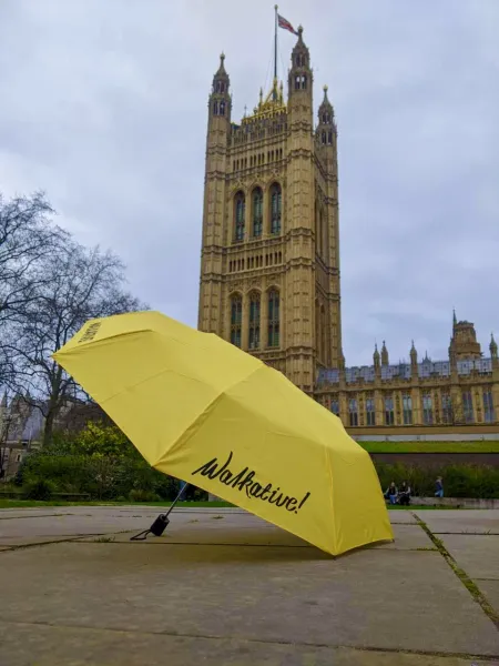 Yellow umbrella with 'Walkative!' logo in front of the Palace of Westminster, London.