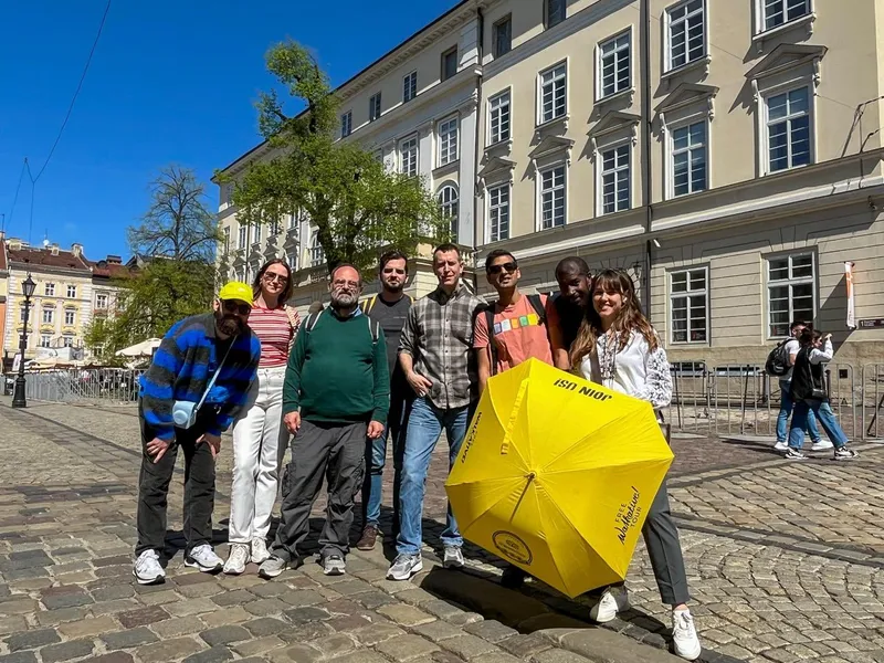 A diverse group of seven people on a cobblestone street in Lviv, with a guide holding a yellow Walkative umbrella in front...