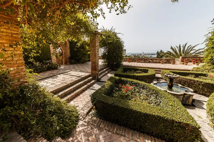 Serene garden in Málaga, Spain, with a fountain and coastal views.