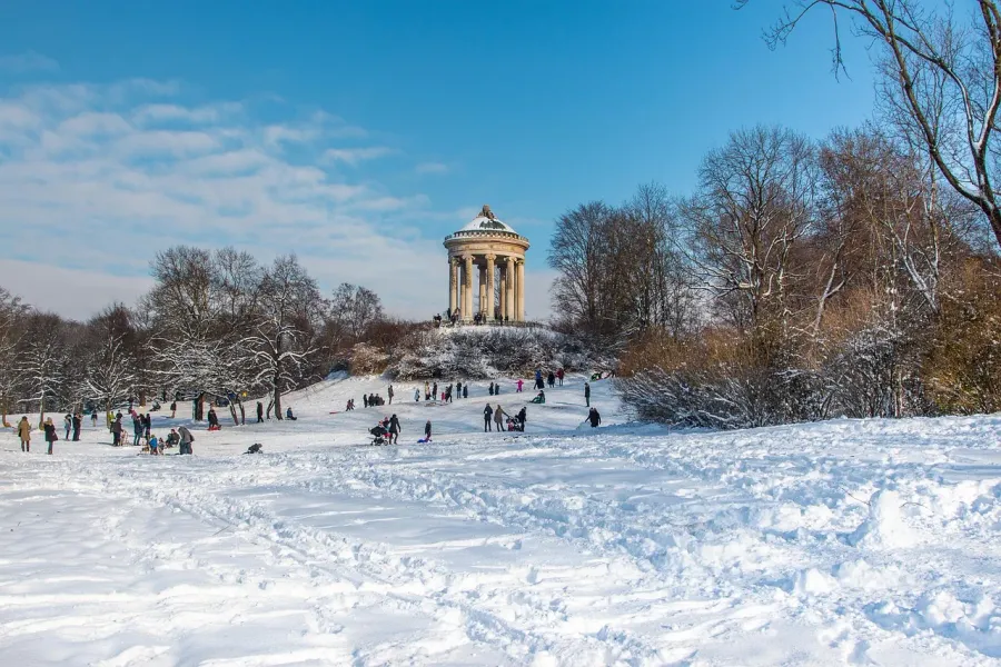 Snow-covered Englischer Garten in Munich with the Monopteros temple and people sledding.