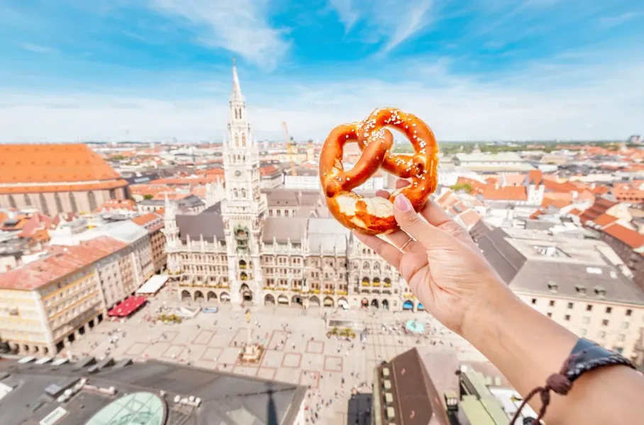 A pretzel held against the backdrop of Munich's Marienplatz.