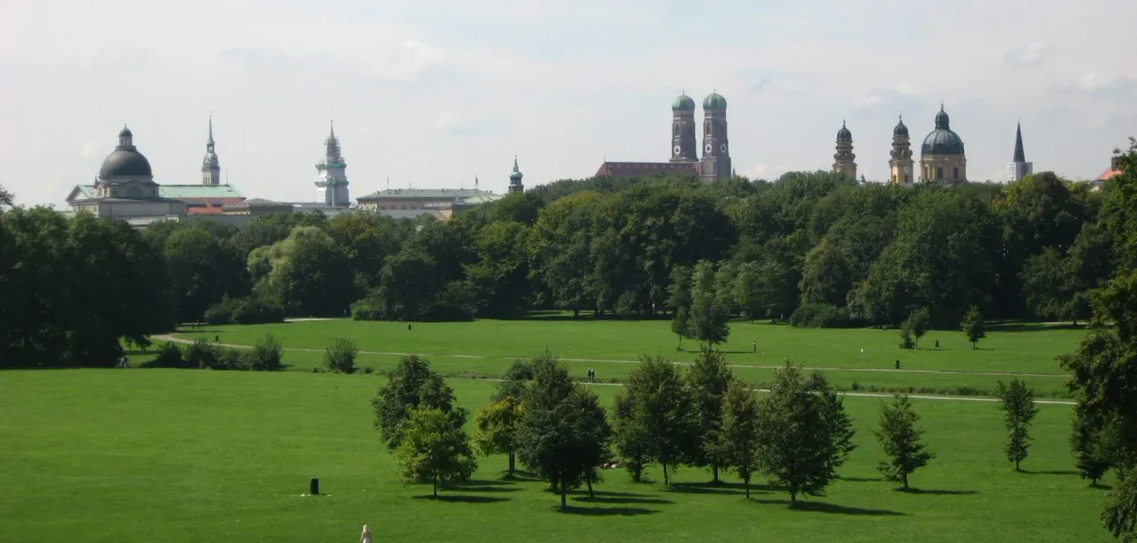 Panoramic view of a green park in Munich, Germany, with the city's skyline visible in the background.