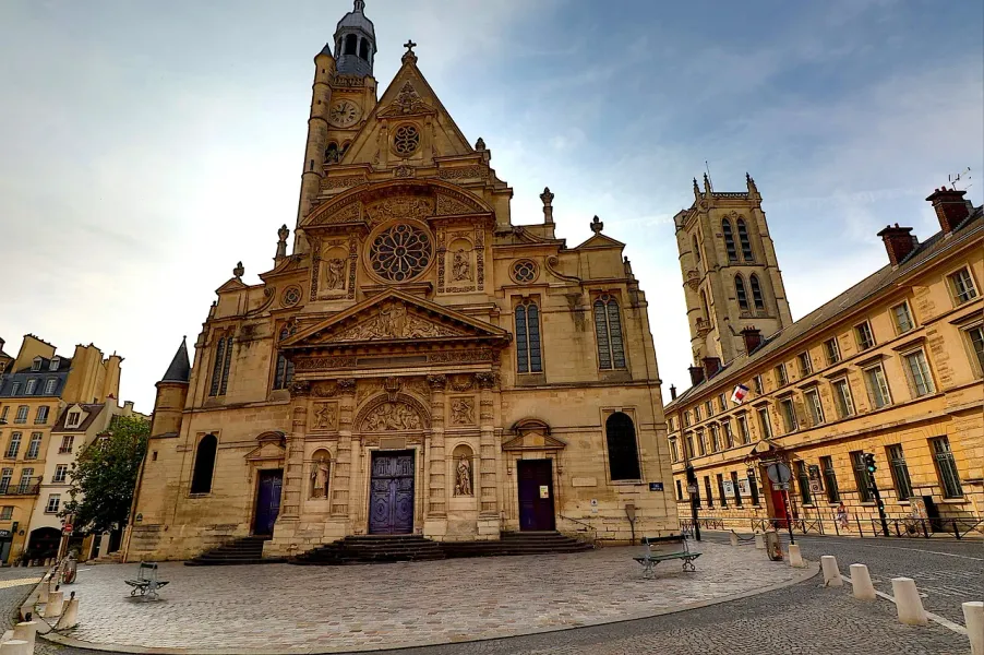 The ornate facade of Saint-Étienne-du-Mont church in Paris, with a clock tower and stained-glass windows, under a partly c...
