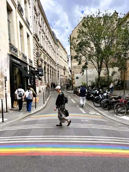 A pedestrian crosses a rainbow crosswalk in a charming Parisian street.