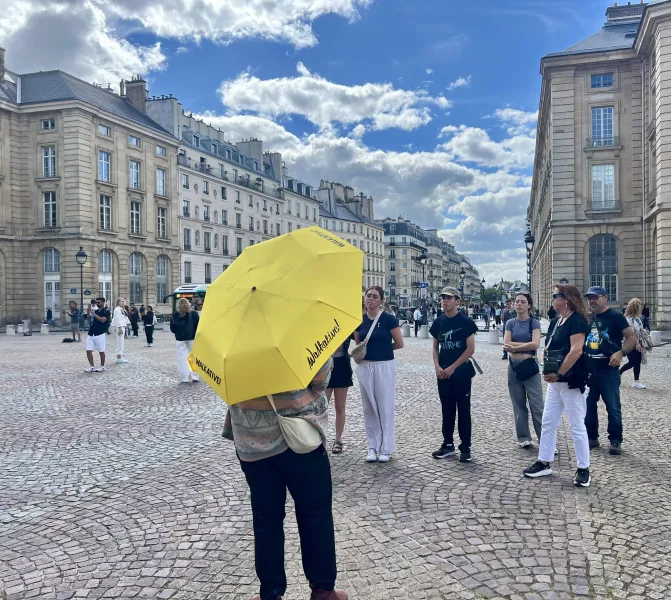 A Walkative! walking tour guide leads a group through a Parisian square.