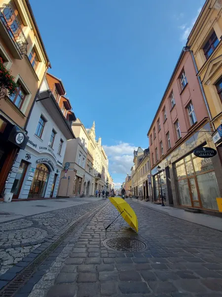 A yellow umbrella lies on a charming cobblestone street in a Polish city, surrounded by historic buildings.