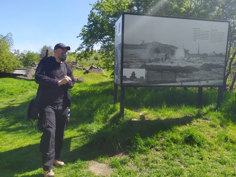 A tourist explores a historical site in Poland, reading an information board with historical photos.