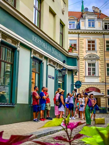 A tour group explores the charming streets of Riga, Latvia, pausing outside a historic restaurant.