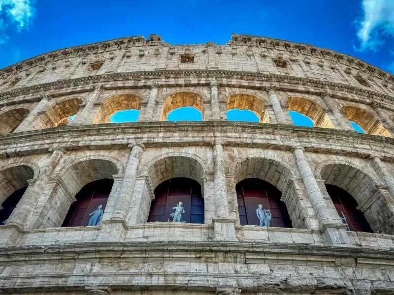 Low-angle view of the Colosseum in Rome, showcasing its impressive architecture and statues.