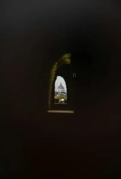 St. Peter's Basilica in Rome, seen through a hedge archway.