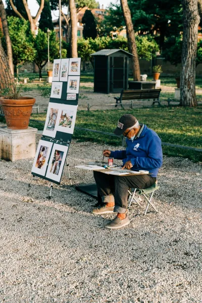 Street artist painting in a Roman park, showcasing artwork depicting famous landmarks.